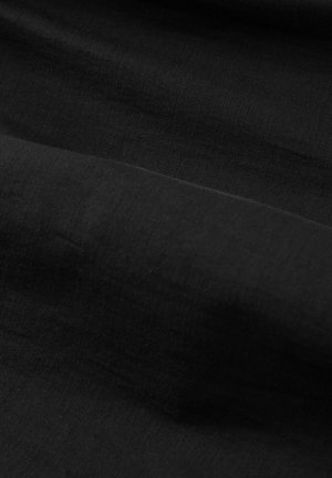 Čierna látka s jemnými záhybmi vytvárajúca subtílny tieň a variácie textúry pod rozptýleným osvetlením.