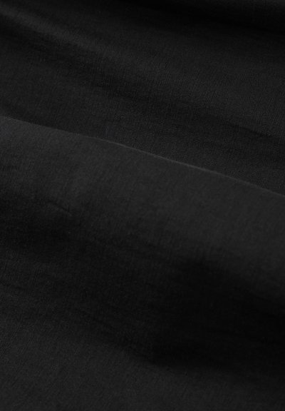 Tissu noir avec des plis doux créant des ombres subtiles et des variations de texture sous un éclairage diffus.