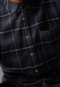 Chemise à carreaux navy avec rayures blanches, col structuré et poche poitrine, fabriquée dans un tissu doux et texturé.