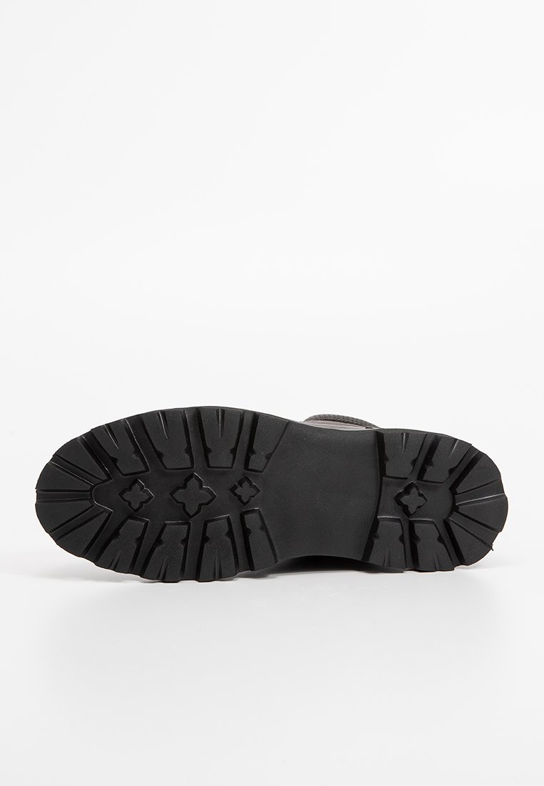 Schwarze Gummisohle mit tiefen Profilen und Mustern, die für Traktion ausgelegt sind. Der obere Rand ist strukturiert und eignet sich für Outdoor-Schuhe.