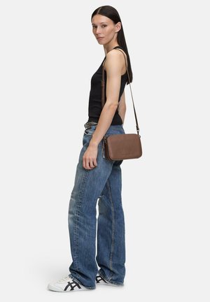 Braune Leder-Crossbody-Tasche mit rechteckiger Form, Reißverschluss und verstellbarem Riemen. Getragen zu hellblauen, weit geschnittenen Jeans und einem schwarzen Tanktop.