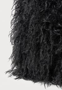Tessuto nero a trama con lunghe fibre ricciolute che creano un aspetto shaggy. Il materiale è denso e appare morbido.
