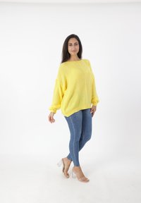Maglione giallo lavorato a maglia con una vestibilità morbida e maniche ampie, abbinato a jeans skinny blu e sandali con tacco a blocco trasparente.