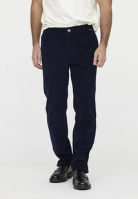 Navy Corduroyhose mit geradem Schnitt, mit einem Frontknopfverschluss und Seitentaschen, kombiniert mit schwarzen Schuhen.