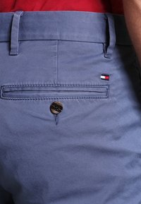 Světle modré bavlněné kalhoty s kapsou na zadní straně, která má jeden knoflík. Malá červenobílo-modrá štítková nálepka poblíž kapsy.