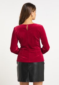 Rød fløjl langærmet bluse med detaljeret nøglehul i ryggen, kombineret med en kort sort læderskirt. Glat tekstur og tætsiddende design.
