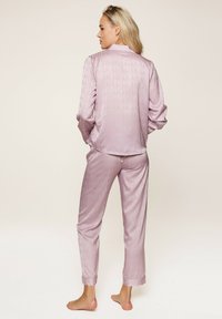 Lavendelfarbene Satin-Pyjamas mit einem dezenten Logomuster, bestehend aus einem Knopf-Oben und Hose mit elastischem Bund, samtiger Textur und aufgerollten Ärmeln.