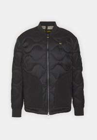 Chaqueta bomber negra con diseño acolchado, textura suave, cierre de cremallera, puños y dobladillo acanalados, con bolsillos laterales y un parche con logo.