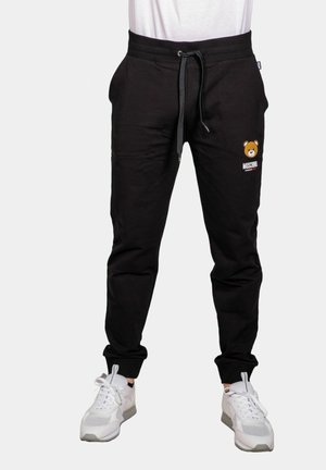 Pantaloni della tuta neri con vita elastica, cordino, tasche laterali e logo dell'orso. Abbinati a sneakers bianche con dettagli in rete.