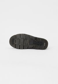 Suela de zapato de goma negra con patrones texturizados y surcos para tracción. Presenta una ligera curva en la punta y una sección de talón reforzada.