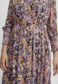 Lange bloemenjurk met paarse, roze en bruine patronen, met een geplooid ontwerp en een riem in de taille. Gemaakt van zachte, gestructureerde stof.