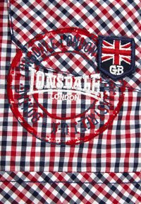 Červená, bílá a modrá kostkovaná tkanina s vyšitým logem "Lonsdale London" a nášivkou britské vlajky. Obsahuje design kulaté razítka.