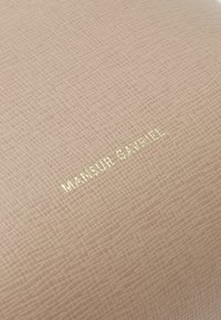 Cuir texturé pêche avec un logo doré en relief "MANSUR GAVRIEL", présentant un motif de grille subtil sur toute la surface.