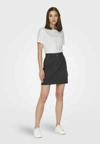 Hvid t-shirt med korte ærmer og en struktureret lomme, parret med en højttalende sort denimnederdel og hvide snøresneakers.