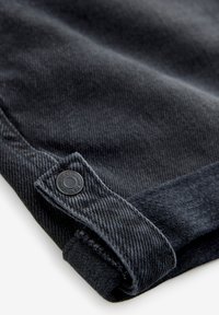 Mörkgrå denimtyg har en vikbar kant med en svart knappdetalj, vilket framhäver en texturerad väv och rena sömnadsdetaljer.