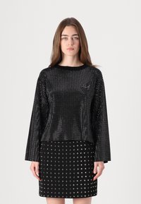 Juoda ilgarankovė palaidinė su taškuotais raštais ir apvaliu kaklu, poruojama su prigludusia sijonu, kuriame taip pat yra sidabro spalvos taškų.