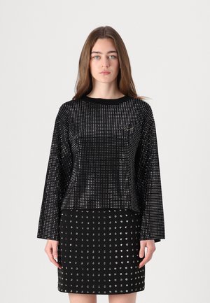 Zwarte langelijngtop met een gestructureerde stof en een ronde halslijn, gecombineerd met een strakke rok met zilveren studs in een vergelijkbaar patroon.