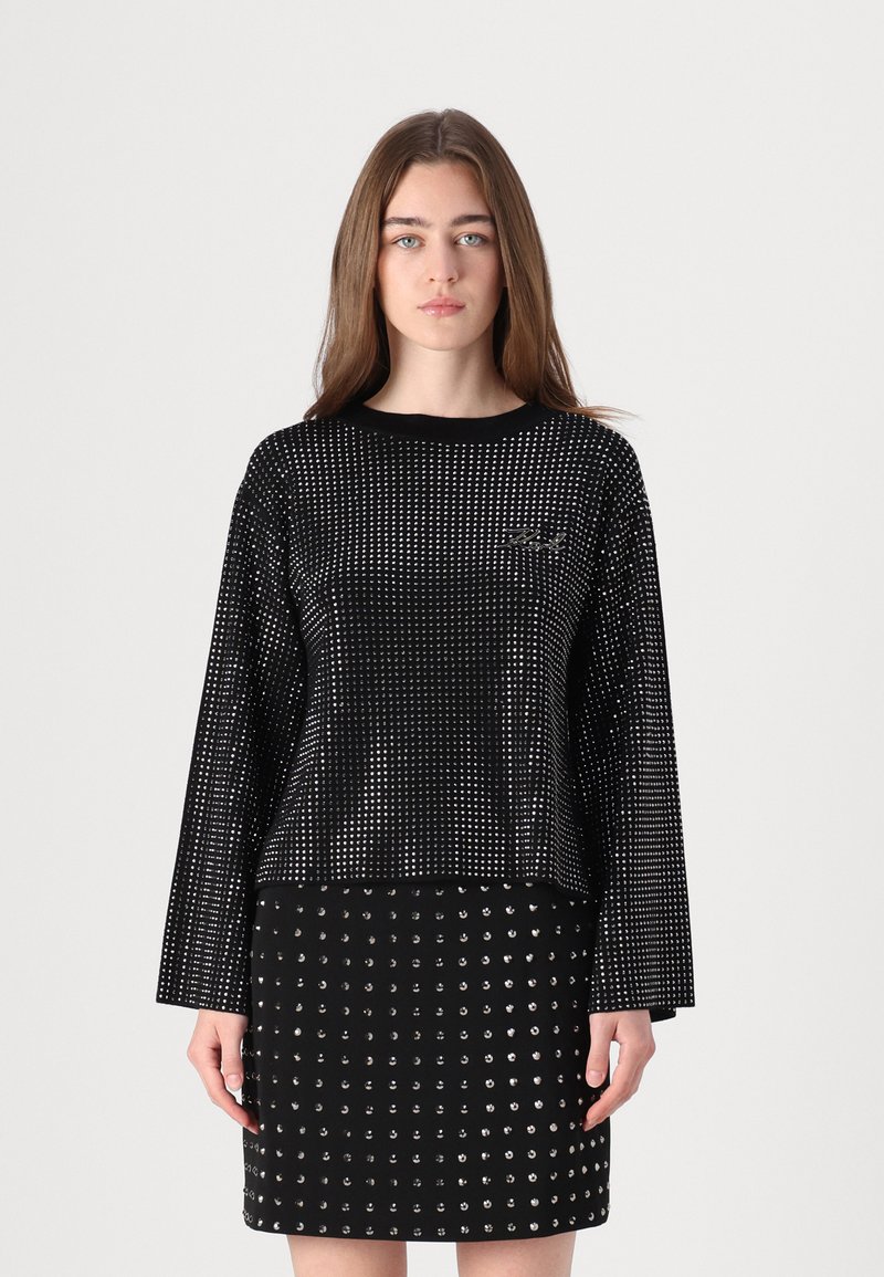 Juoda ilgarankovė palaidinė su taškuotais raštais ir apvaliu kaklu, poruojama su prigludusia sijonu, kuriame taip pat yra sidabro spalvos taškų.