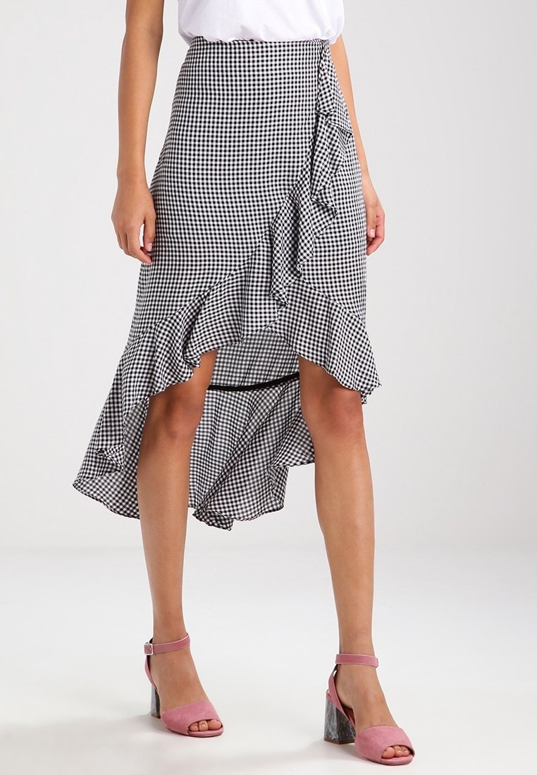 Schwarz-weißer Karorock mit asymmetrischem Saum und Rüschendetail, kombiniert mit rosa Absatzsandalen. Glatte Stoffstruktur.