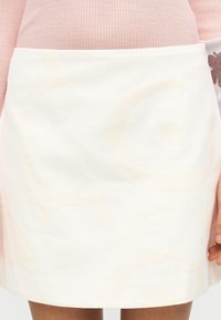 Λευκή φούστα με υφή, με μεγάλα, διακριτικά αφηρημένα σχέδια σε πιο ανοιχτή απόχρωση. Σχεδίαση με ίσια γραμμή, μήκος μέχρι τη μέση του μηρού.