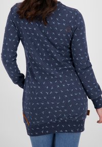 Top de manga larga azul marino con un patrón de pájaros en azul claro, puños acanalados y un parche de acento lateral. Material de algodón suave.