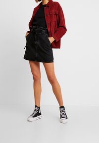 Röd kordjacka, svart t-shirt, högmidjad svart denimkjol och svarta högtoppsskor med vita sulor. Enkelt design och texturer.