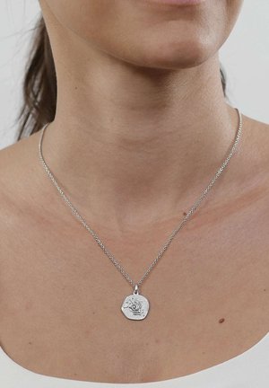Silver necklace with a round irregular pendant featuring an embossed hand and star design on a person’s neck and upper chest.