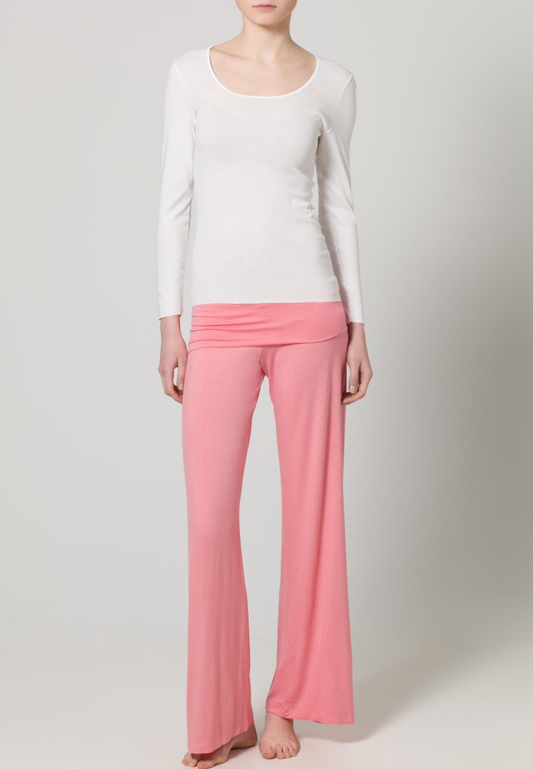 Hvid langærmet top med scoop-neckline, parret med rosa buks med vide ben lavet af blødt stof, med en foldet talje.
