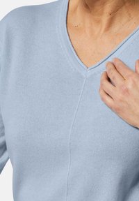 Hellblauer Pullover mit V-Ausschnitt, hergestellt aus einem weichen Strickstoff. Verfügt über eine strukturierte Oberfläche und sichtbare Nähte entlang der Säume.