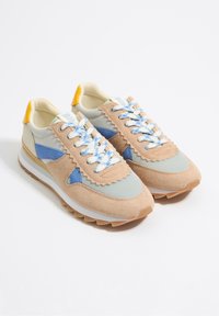 Zapatillas multicolores con una combinación de gamuza beige, tela azul claro y acentos en verde menta. Suela de goma blanca y cordones azules.