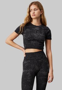 Top corto nero strutturato con maniche corte e collo rotondo, abbinato a leggings neri a vita alta. Logo sul petto.