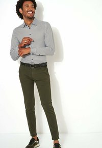 Langarmshirt met een wit en zwart stippenpatroon, gecombineerd met olijfgroene broek en zwarte sneakers met accenten.