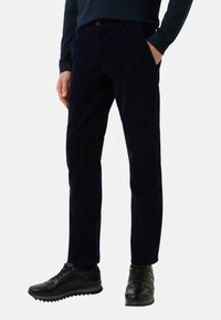 Mørkeblå kordbukser med lige pasform, frontlommer og knaplukning, sat sammen med sorte sportsko.