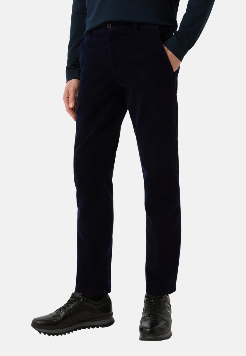 Mørkeblå kordbukser med lige pasform, frontlommer og knaplukning, sat sammen med sorte sportsko.