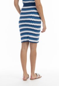 Enges Kleid mit Zickzackmuster in Blau und Weiß, gerippter Taillenbereich, knielang, kombiniert mit weißen Slipper-Sandalen mit strukturiertem Detail.
