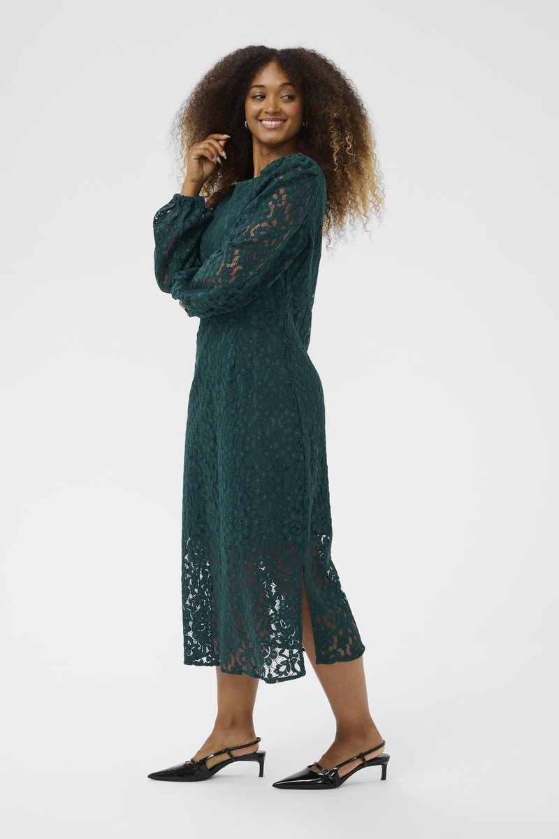 Lace long-sleeve dress in dark green, featuring floral patterns, a mid-length hem with side slits, paired with black heeled shoes.