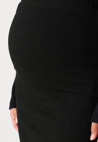 Crna rebrasta suknja s prilagođenim siluetom, s vertikalnim linijama i glatkom teksturom. Ima visoki pojas i dužinu do koljena.