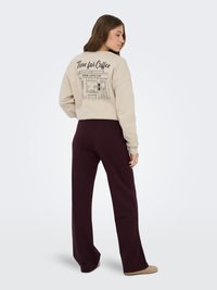 Femme portant un sweat-shirt beige avec l'inscription "Time for Coffee" et une illustration de café au dos, associée à un pantalon large marron foncé.