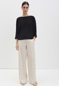 Top nero ampio con scollo alla barca, abbinato a pantaloni beige a gamba larga e tacchi con cinturini. Tessuto liscio e linee pulite sono evidenti.