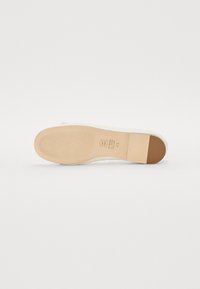 Lys kremfarget såle til sneakers med en teksturert gummiunderbunn, med en tan-farget hælrekke og ruggede overflate for grep.