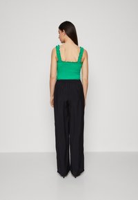 Top à bretelles froncé vert avec des volants, associé à un pantalon noir ample. L'ensemble présente une coupe décontractée et une texture lisse.