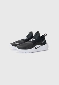 Baskets de sport noires avec une tige texturée, une sangle élastique portant "NIKE", et une semelle en caoutchouc blanche. Conçues pour le confort et la facilité d'utilisation.