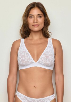 Bralette en dentelle blanche avec un décolleté en V profond, ornée de motifs floraux. Les bretelles sont larges et la texture est transparente et délicate.