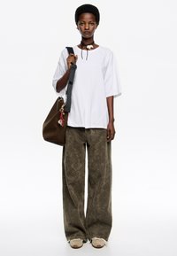 Camiseta blanca de gran tamaño, pantalones amplios de estampado verde oliva, zapatillas beige, bolso marrón con accesorios y collar choker.