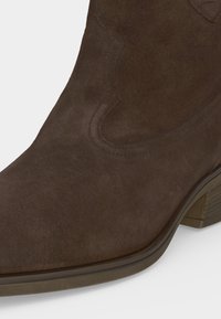 Bottine en daim marron avec un bout arrondi, des détails de couture subtils et un petit talon en bois empilé.