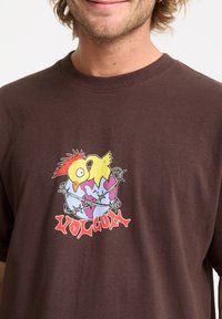 Brun kortærmet t-shirt lavet af bomuld, der har et farverigt grafik med en tegneserie fugl og en globe, med "VOLCOM" tekst i rød.