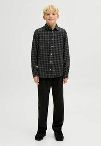 Melnā un baltā šaha raksta garpiedurkņu krekls ar pogājamo apkakli, valkāts kopā ar melnām biksēm un melnām kurpēm. Gluda auduma tekstūra.