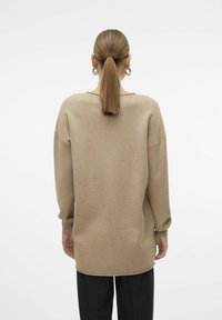 Beiger, oversized Pullover mit langen Ärmeln, strukturiertem Strick, abgerundetem Saum und lässiger Passform, von hinten betrachtet.