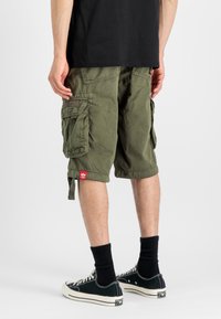 Olivenfargede cargoshorts laget av bomull, med sidelommer, justerbare sømmer og et vevd merke på venstre lår, kombinert med svarte sokker og joggesko.