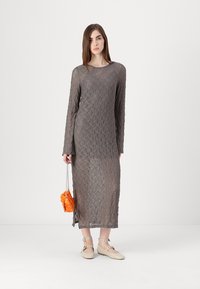 Vestido longo de renda cinza com um padrão detalhado e fenda lateral, combinado com uma bolsa laranja e sapatos de tiras bege.